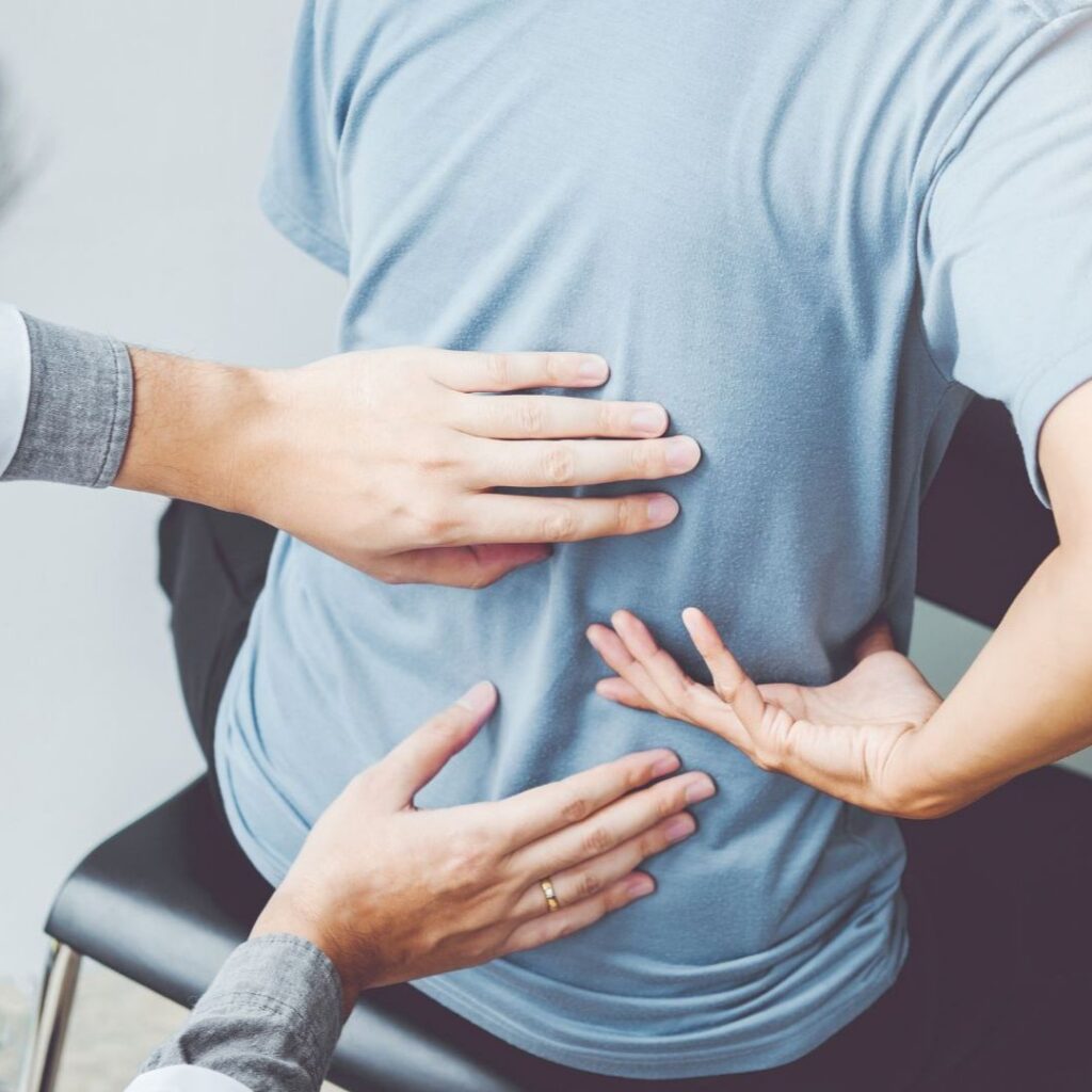 A close-up view from behind of a patient in a light blue t-shirt receiving a physical exam or chiropractic adjustment on their back.